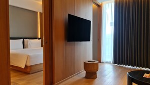Una habitación de hotel con cama, televisión montada en la pared, piso de madera y ventana con cortinas.