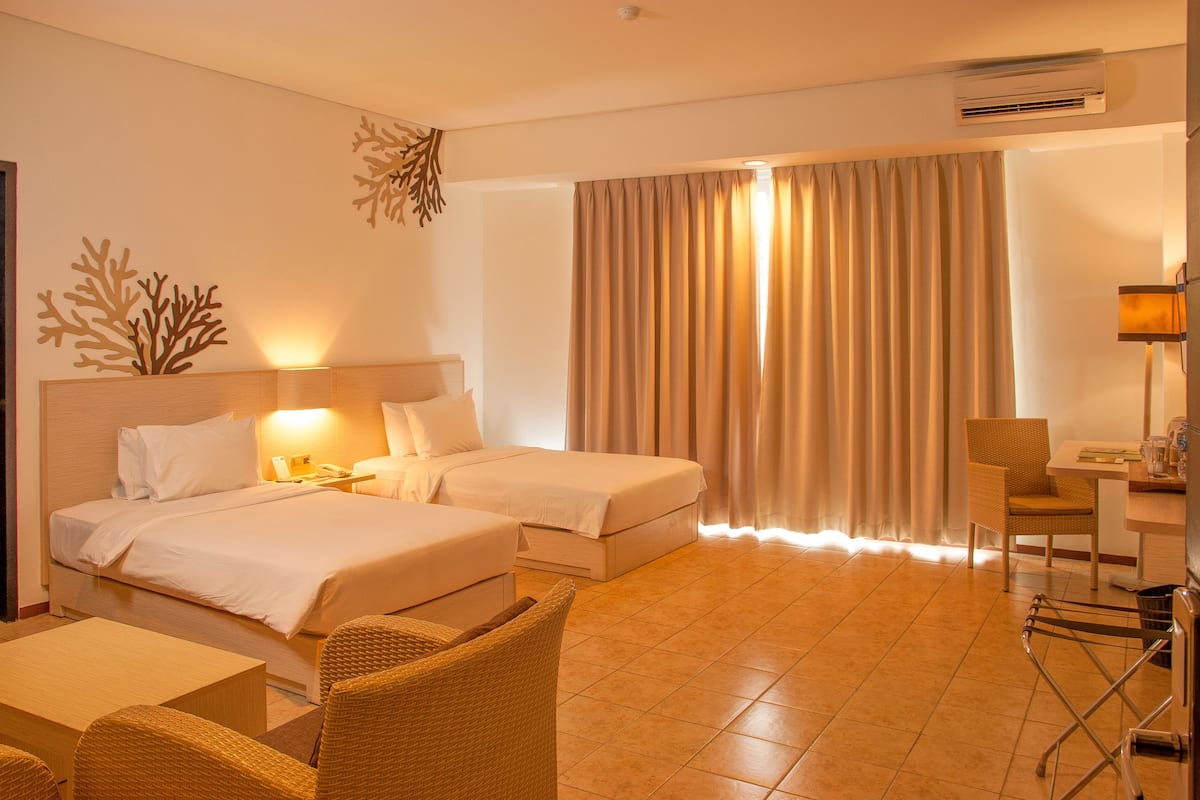 Habitación de hotel con dos camas, un escritorio, una silla y un aire acondicionado de pared.