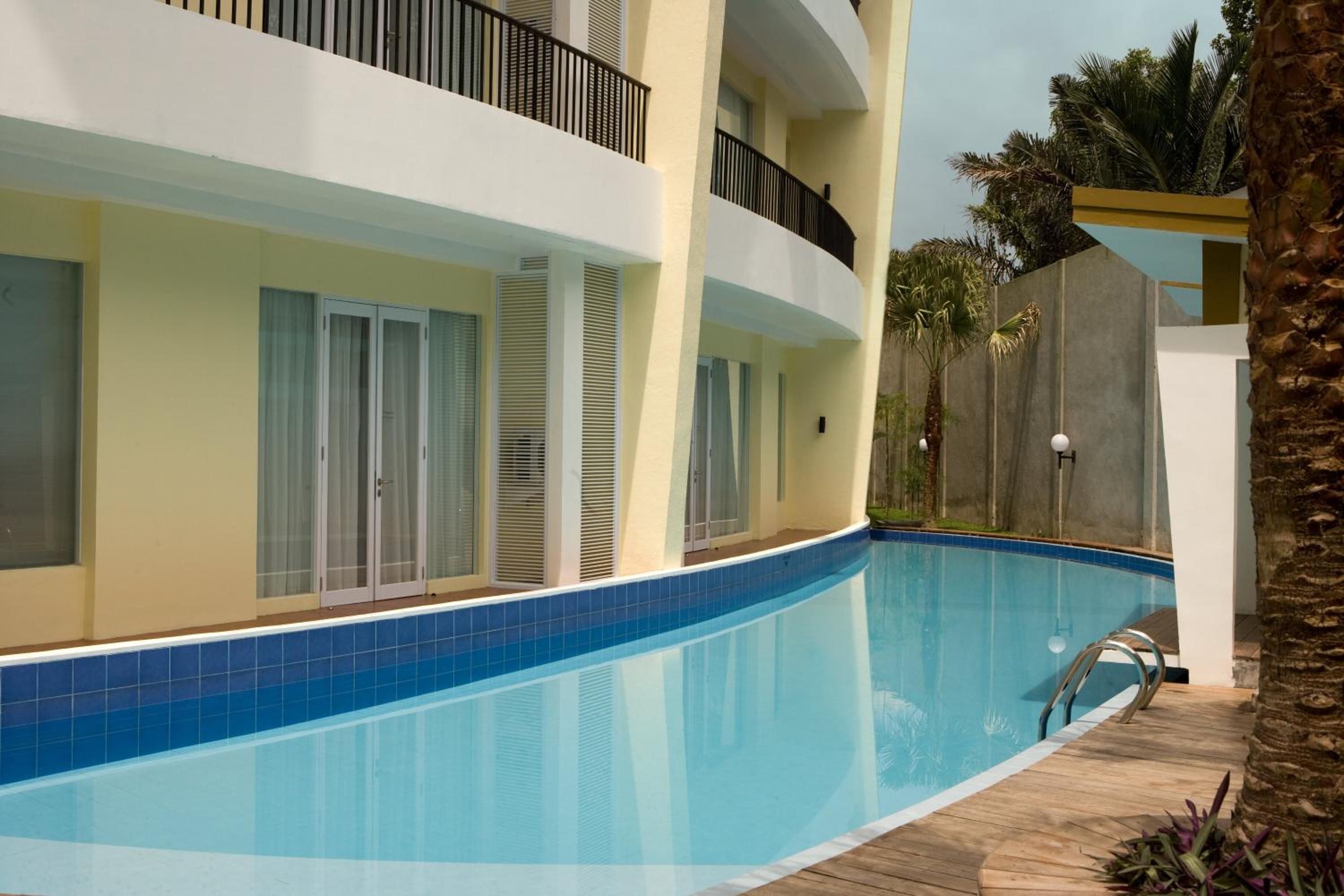A swimming pool with a wooden deck, a palm tree, and a building with balconies and windows.