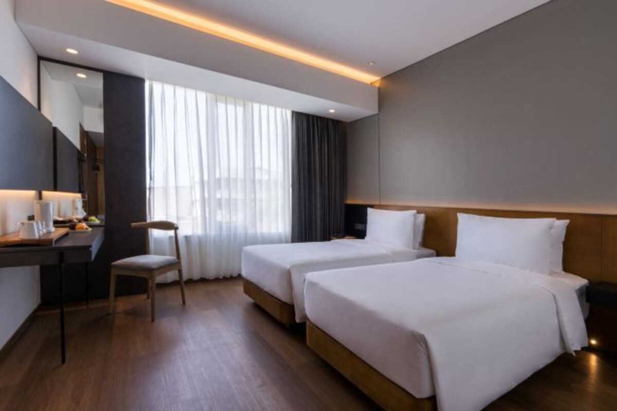 A hotel room with two beds, a desk with a chair, and a large window with curtains.