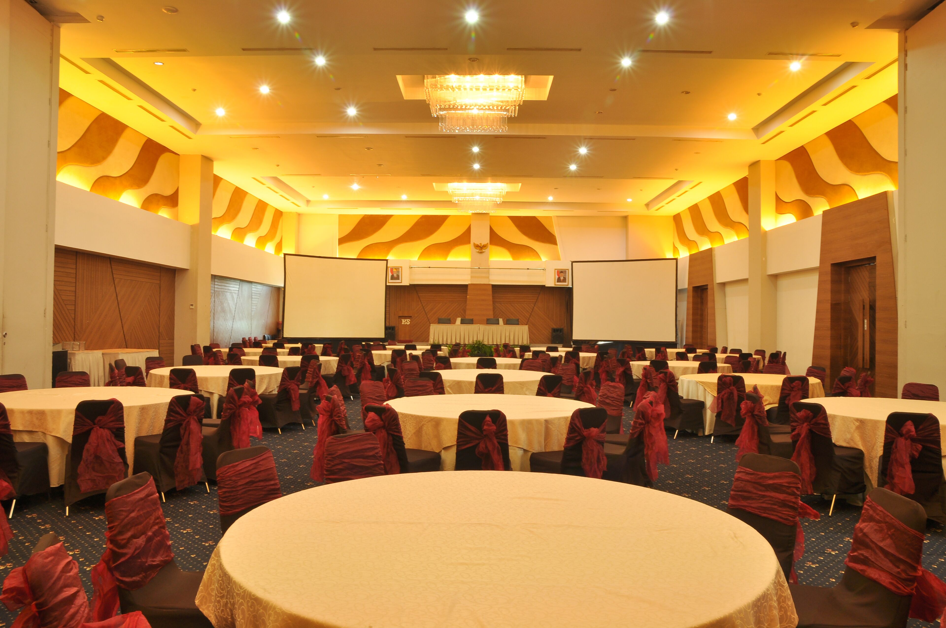 Un salón de conferencias con varias mesas redondas, sillas con cintas rojas y una gran lámpara de araña.