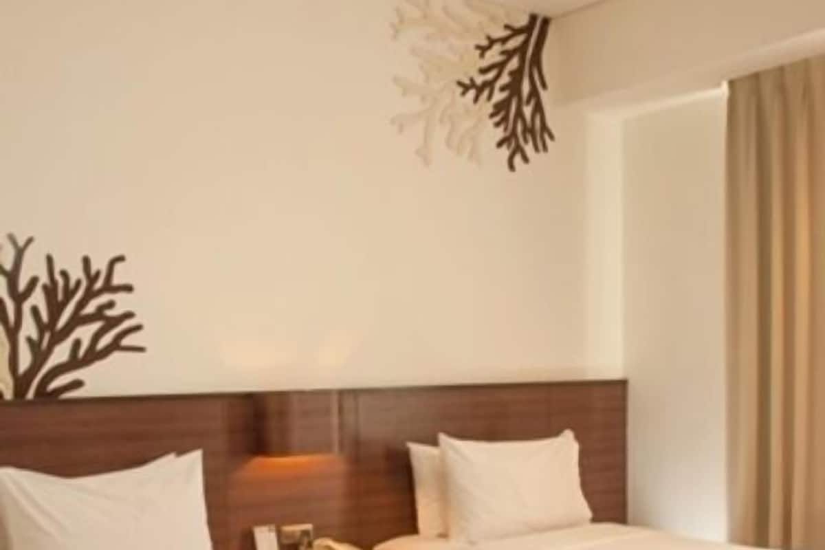 Habitación de hotel con dos camas, cabecero de madera, un adorno en la pared y una ventana con cortinas.