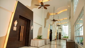 Un amplio vestíbulo de hotel con techos altos, ventiladores de techo y grandes ventanales que dejan entrar luz natural.