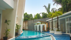Una piscina de diseño curvo, rodeada de plantas en macetas y palmeras.