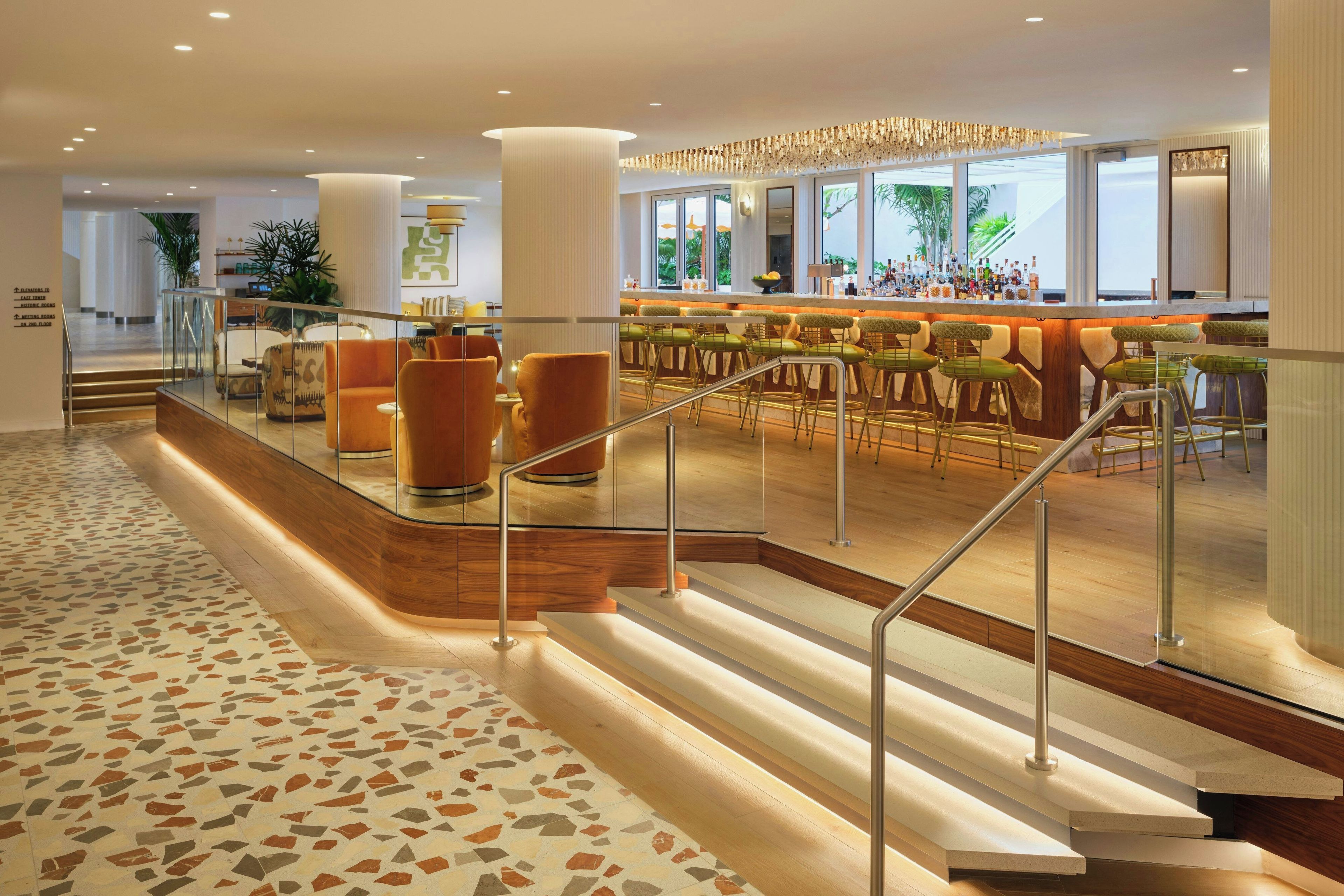 Un vestíbulo de hotel con área de bar, asientos y una escalera.