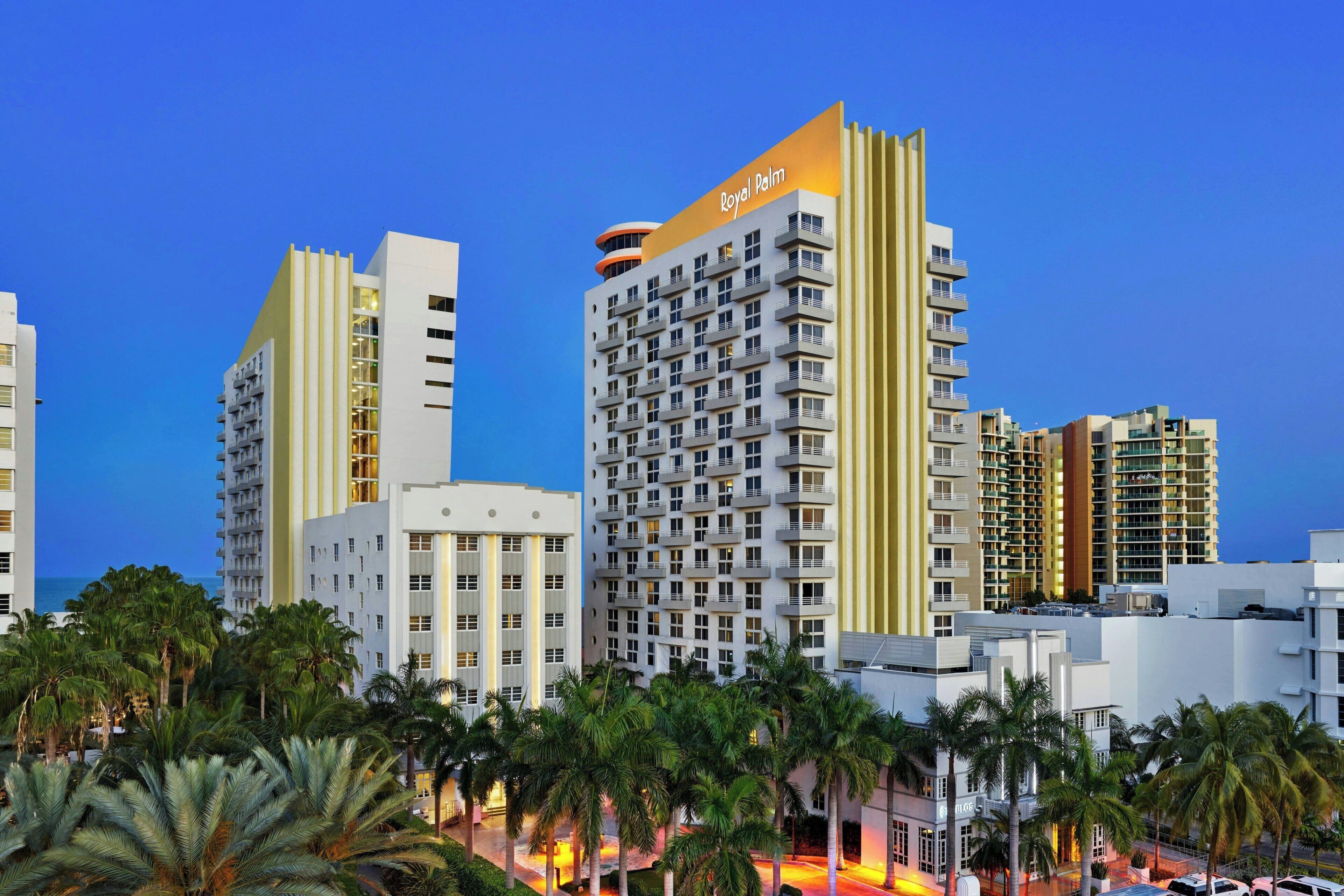 A high-rise hotel with multiple balconies, a prominent 'Royal Palm' sign, and a view of the ocean.