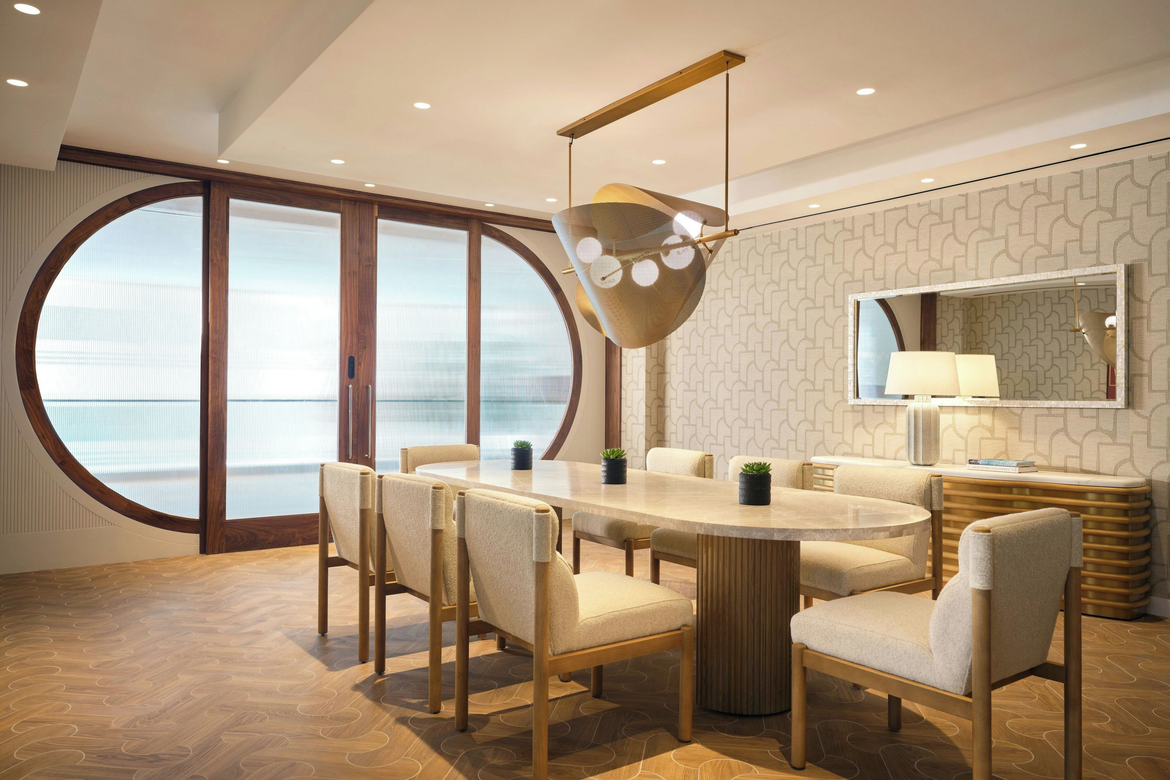 Uma sala de jantar moderna com uma mesa redonda, cadeiras, luminária pendente e uma janela grande com vista.