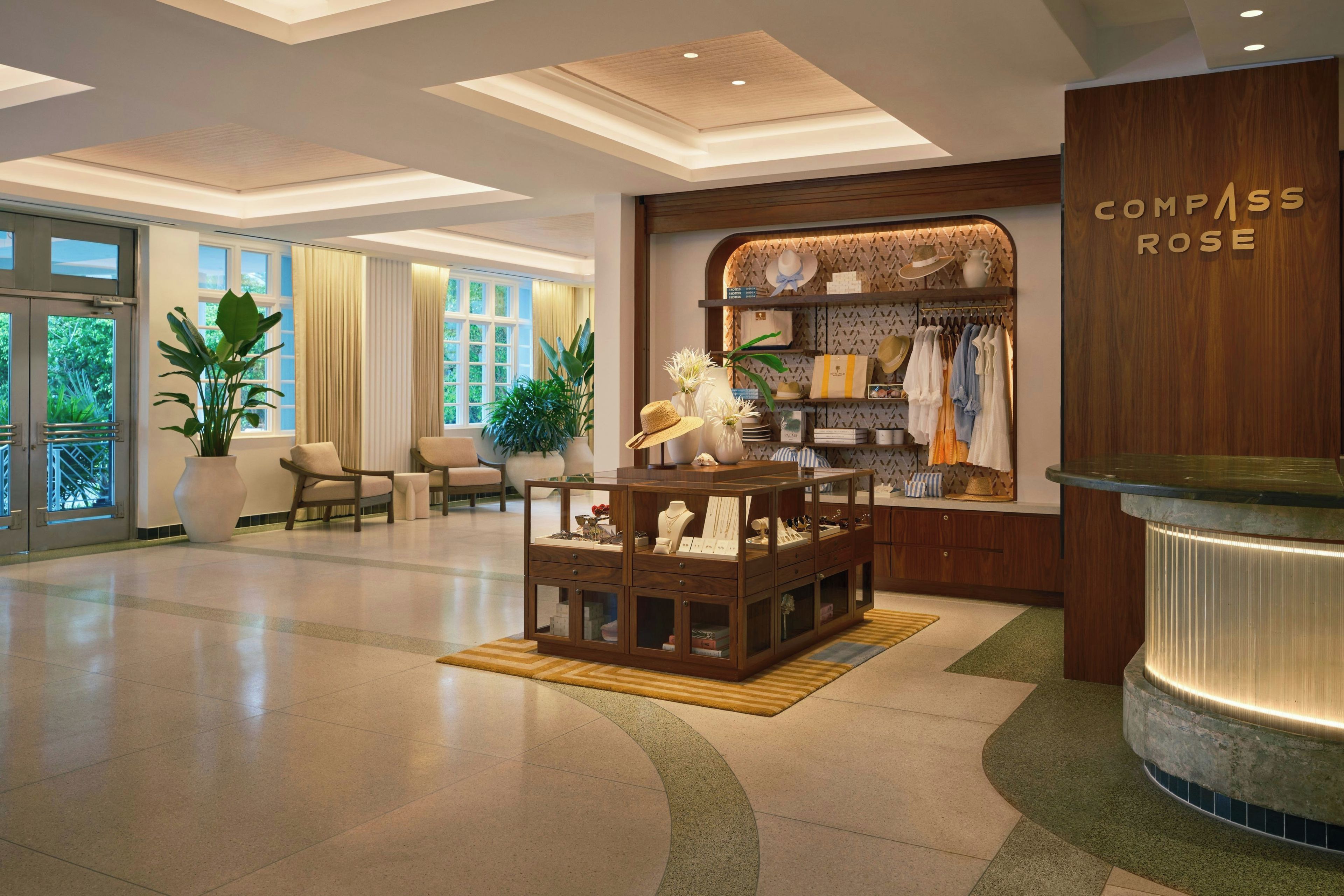 Een hotel lobby met een receptiebalie, een zithoek en een winkel genaamd 'Compass Rose'.