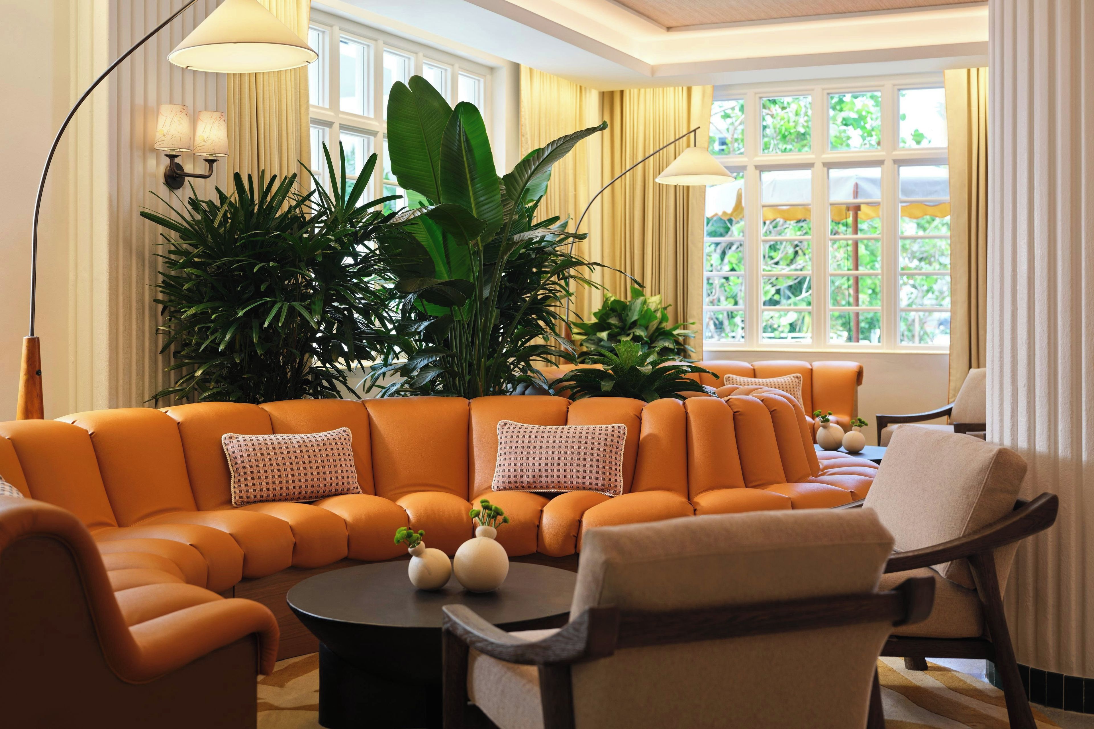 A modern living room with a sectional sofa, a round coffee table, and multiple potted plants.