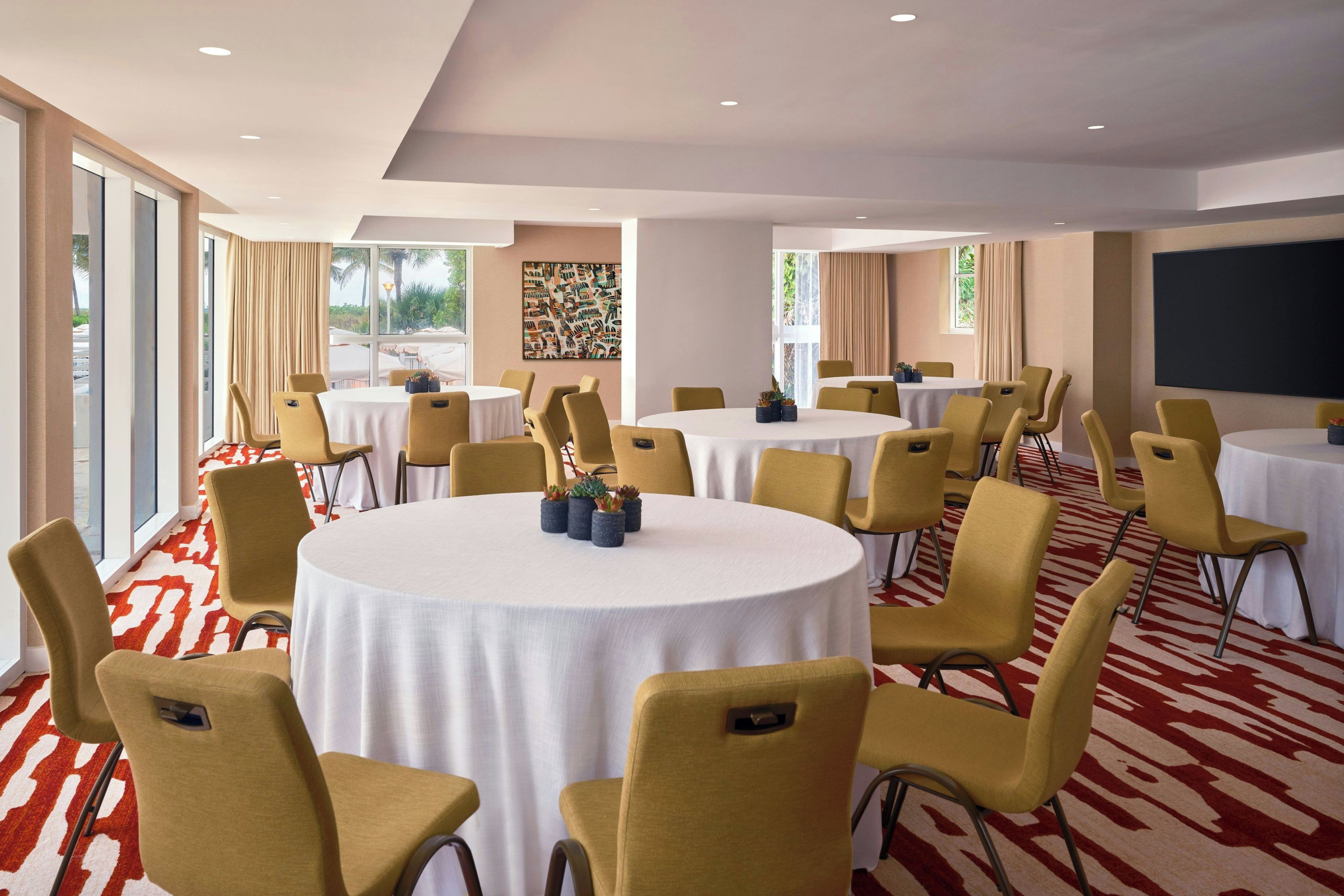A conference room with multiple round tables, yellow chairs, and a red and white patterned carpet.