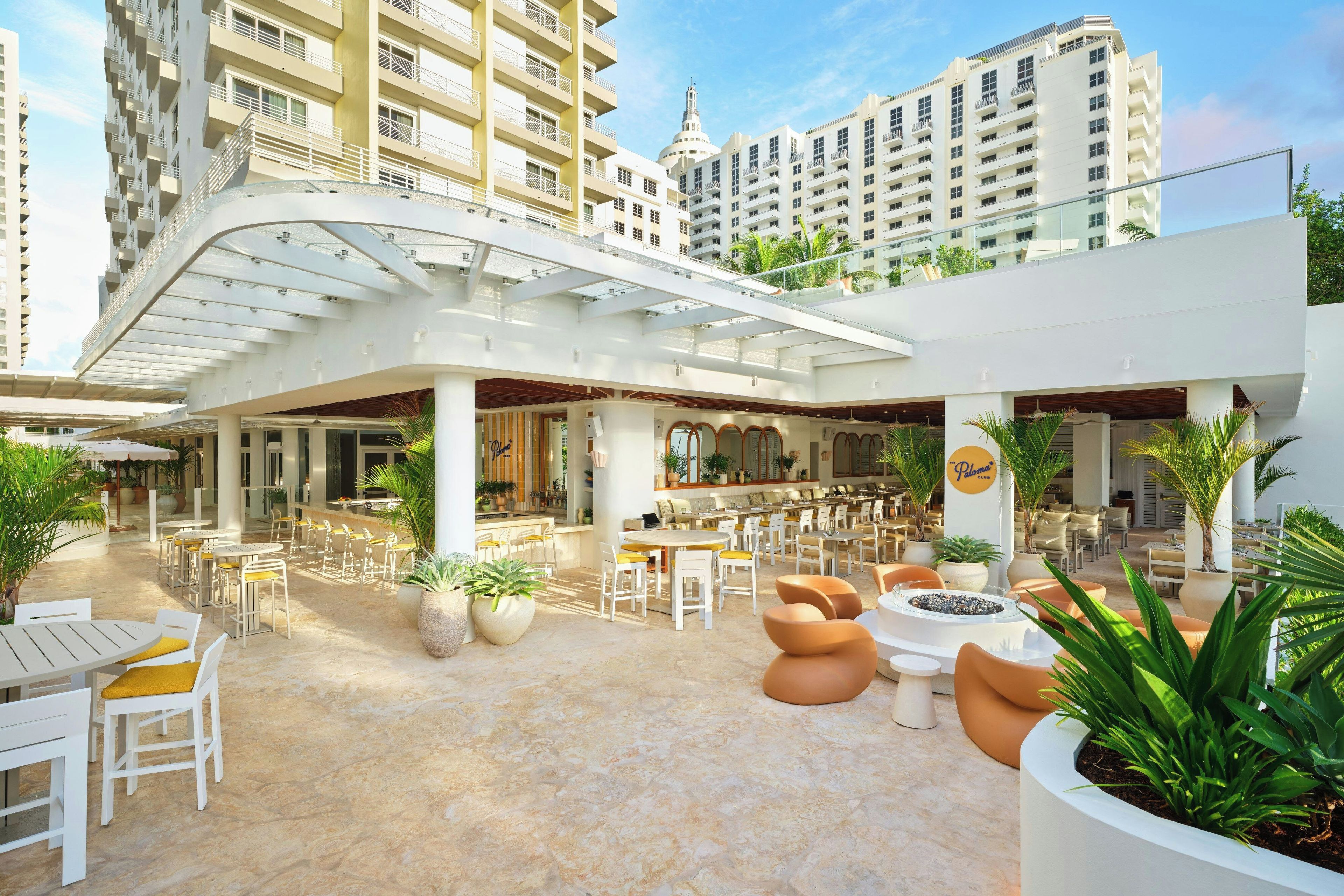 A rooftop bar with outdoor seating, surrounded by high-rise buildings.
