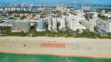 A coastal cityscape with high-rise buildings, a beach with sun loungers, and a marina in the background.