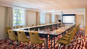 A conference room with a long table, chairs, a projector screen, and windows with curtains.