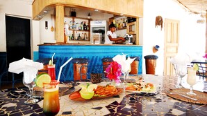 A bar area with a blue tiled counter, a refrigerator, and various bottles. There are drinks on the table, including a cocktail with a lime wedge. - Blue Africa (Mbour)