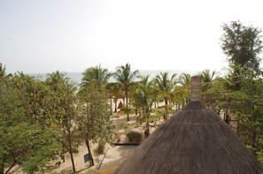 A thatched-roof hut surrounded by palm trees and a sandy beach. - Blue Africa (Mbour)