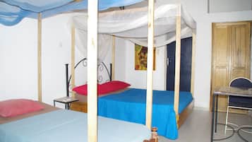 A room with two beds, each with a canopy, a small table, and a chair.