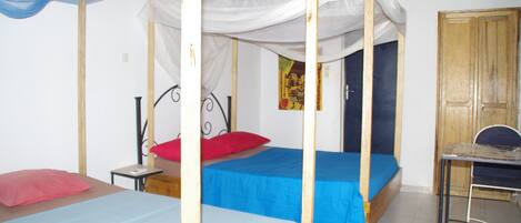 A room with two beds, each with a canopy, a small table, and a chair.