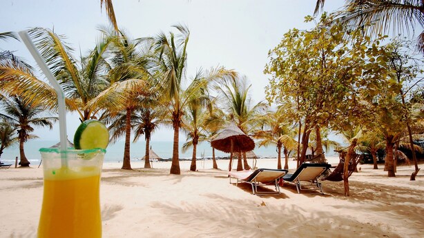 A beach with palm trees, a straw in a drink, and a beach umbrella. - Blue Africa (Mbour)