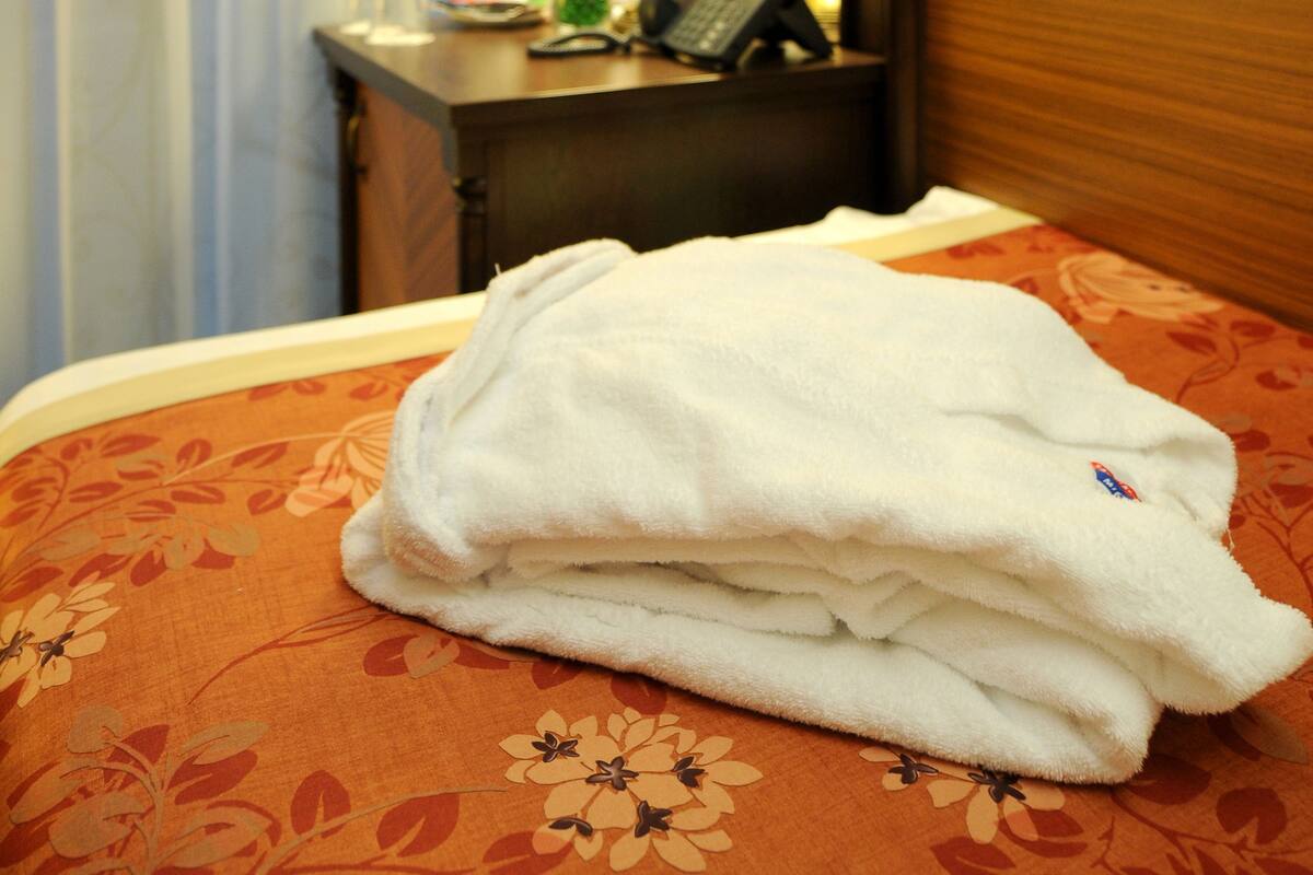 A hotel room with a bed, a bedside table with a lamp, a telephone, and a folded towel.