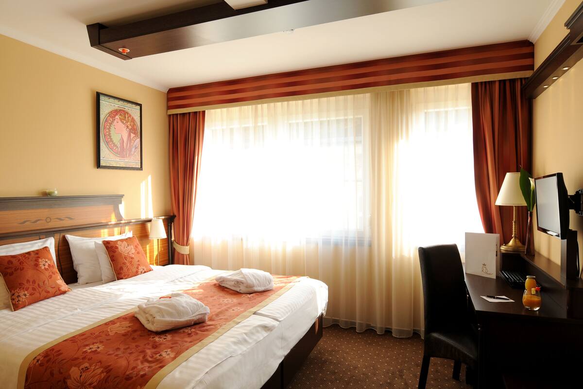 A hotel room with a large bed, a desk, a chair, and a window with curtains.