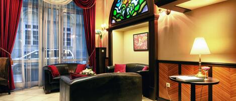 A hotel room with a large window, a sofa, a small table with a lamp, and a decorative wall panel.