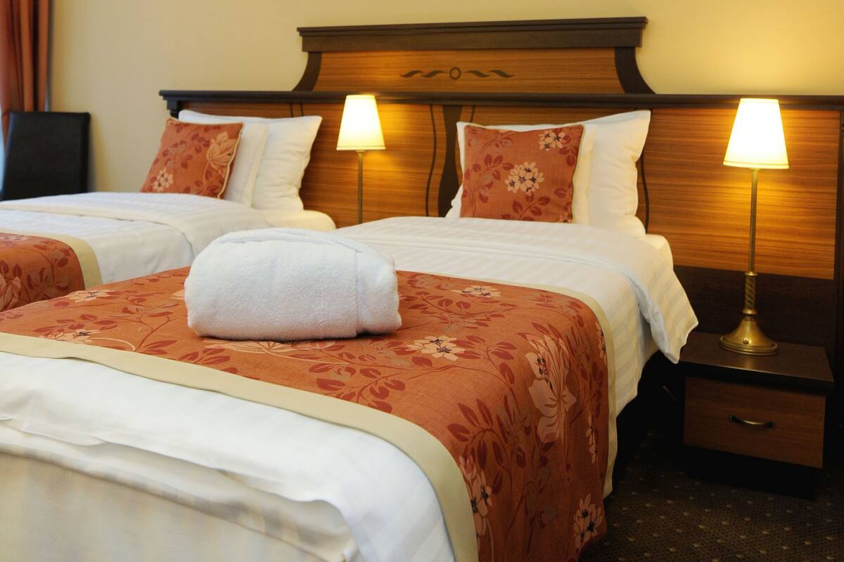 A hotel room with two beds, floral bedspreads, matching lamps, and two framed artworks on the wall.
