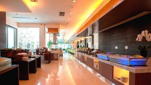 A modern hotel lobby with a long reception desk, a buffet area, and a seating area with tables and chairs. - Hotel Santika Bogor (Bogor)