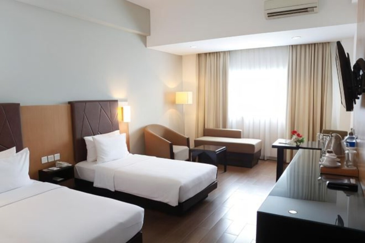 Habitación de hotel con dos camas, un escritorio, una silla, un sofá y un ventanal con cortinas.