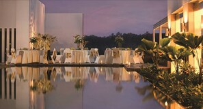 A poolside dining area with tables set for guests, surrounded by lush greenery and a calm evening sky. - Hotel Santika Bogor (Bogor)