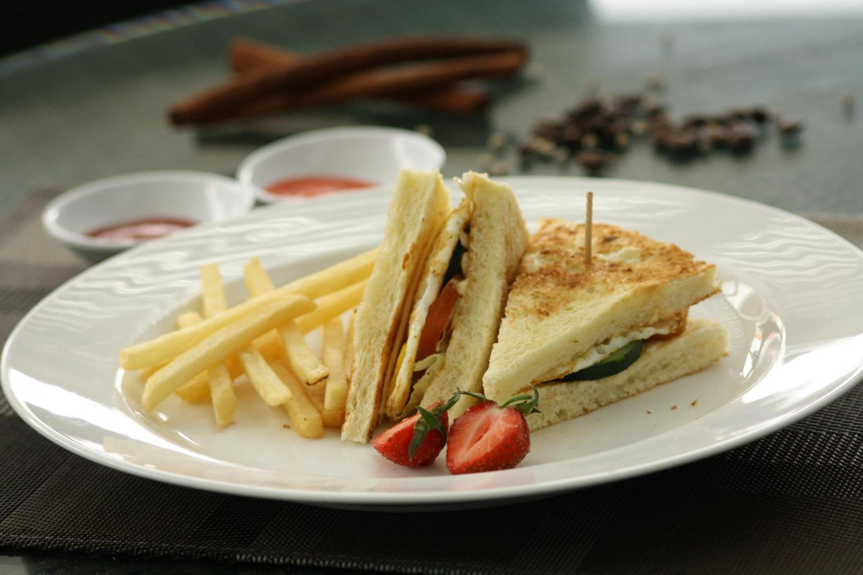 A plate with a sandwich, fries, and a strawberry.