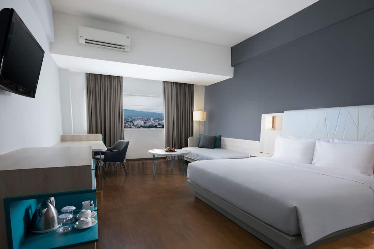 A modern hotel room with a large bed, a desk, a chair, a small table, and a TV.