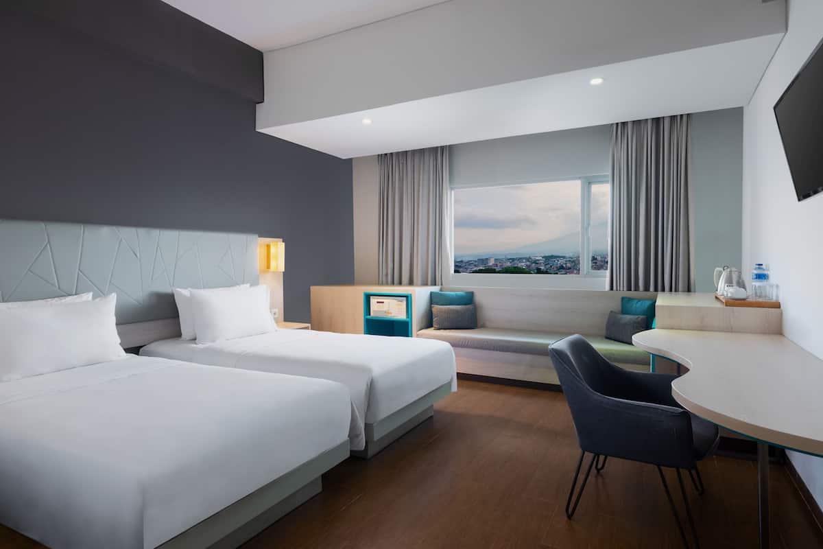 A modern hotel room with two beds, a seating area with a view, and a dining table.