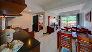 A modern kitchen with a dining area, a small kitchenette, and a view of a garden through large windows. - Krabi Apartment Hotel (Krabi)