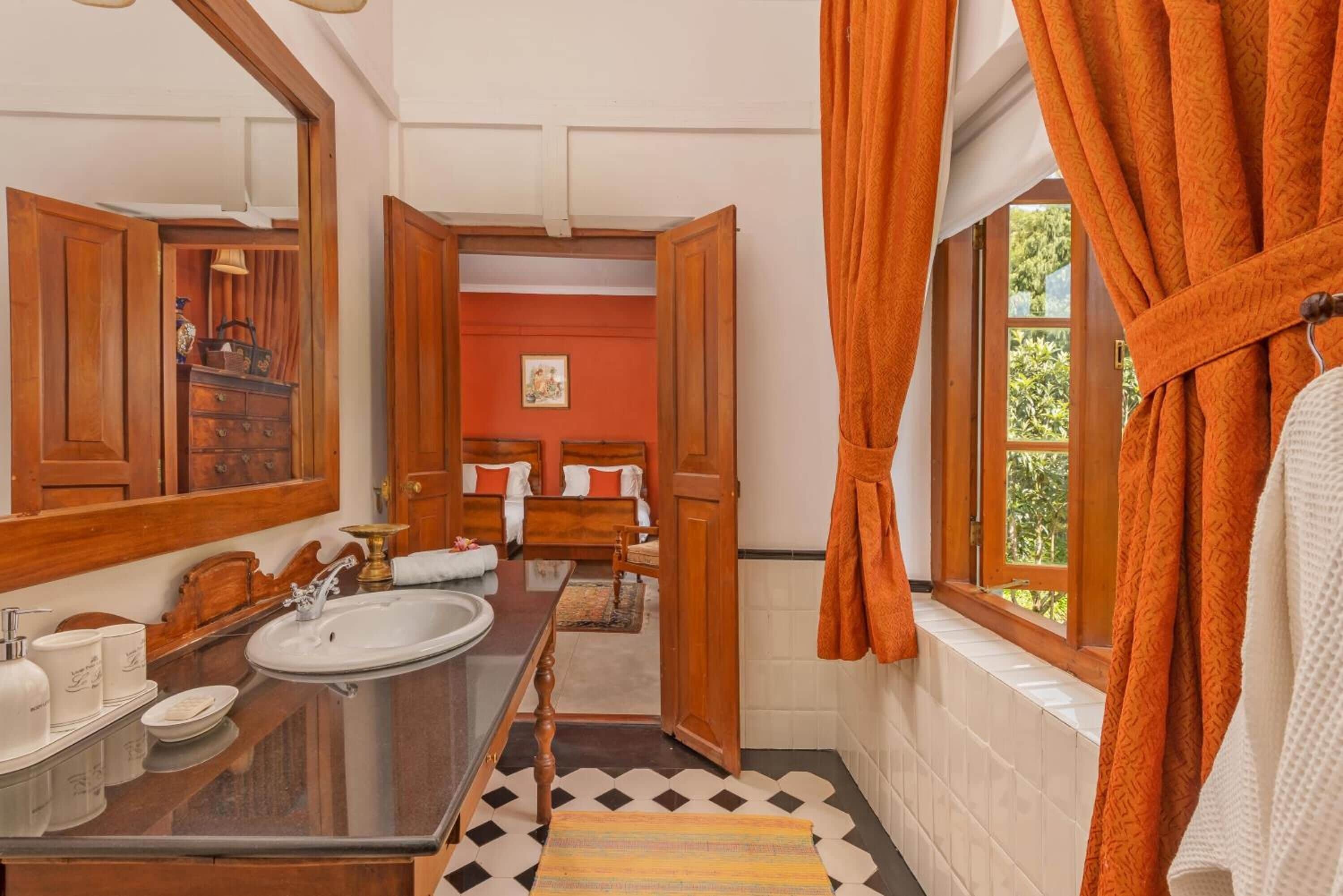 Un bagno con un mobile bagno in legno, uno specchio grande, un lavandino e una finestra con tende arancioni.