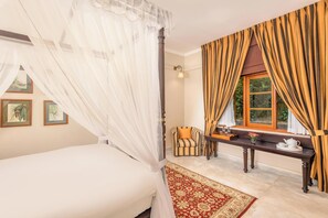 A bedroom with a canopy bed, a window with curtains, a bedside table with a teapot, and a chair.
