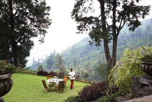 A dining area with a table set for two, surrounded by lush greenery and trees.
