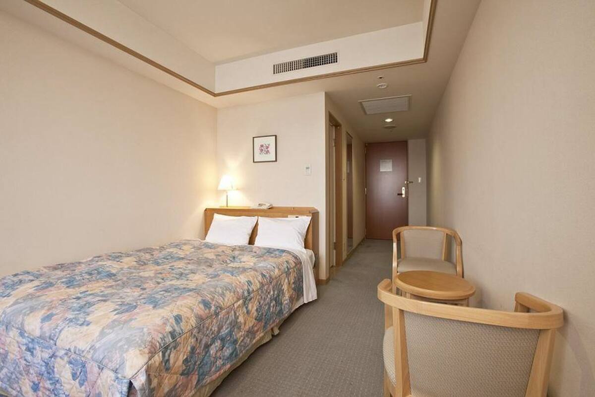 Hotellihuone, jossa on sänky, tuoli ja pieni pöytä.