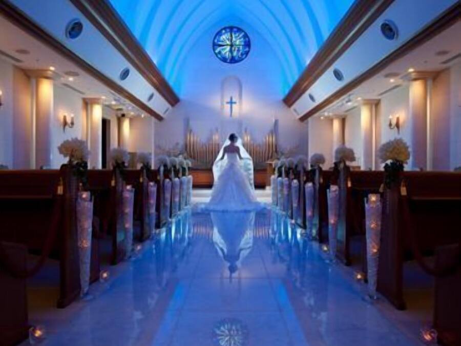 A church interior with pews, a central aisle, and a stained glass window.