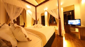 A hotel room with a large bed, curtains, a television, and wooden flooring. - Era Beach (Unawatuna)