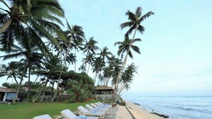 A beach with lounge chairs lined up on a stone pathway, palm trees, and a small hut in the background. - Era Beach (Unawatuna)