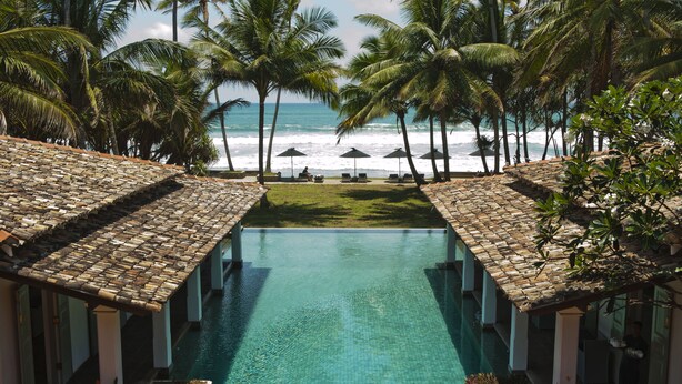 A pool with a tiled floor, surrounded by palm trees and a view of the ocean. - Era Beach (Unawatuna)