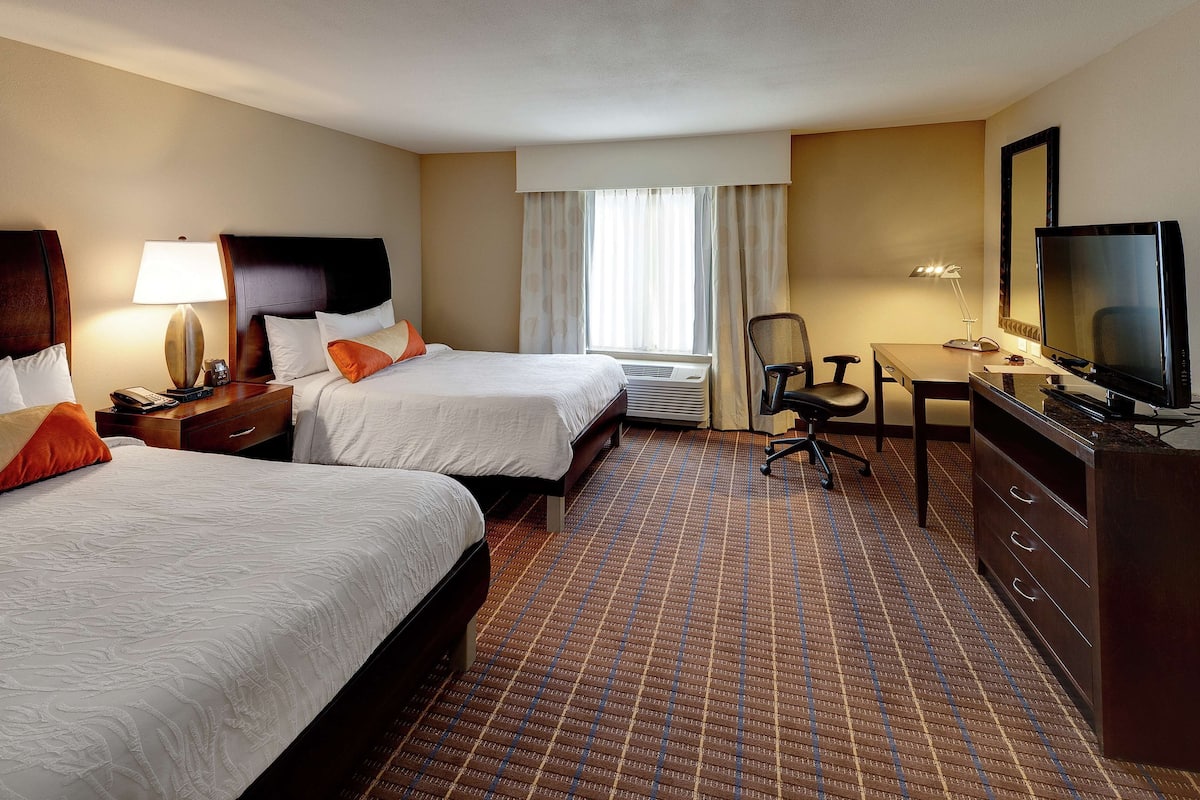 A hotel room with two beds, a desk, a TV, and a chair.