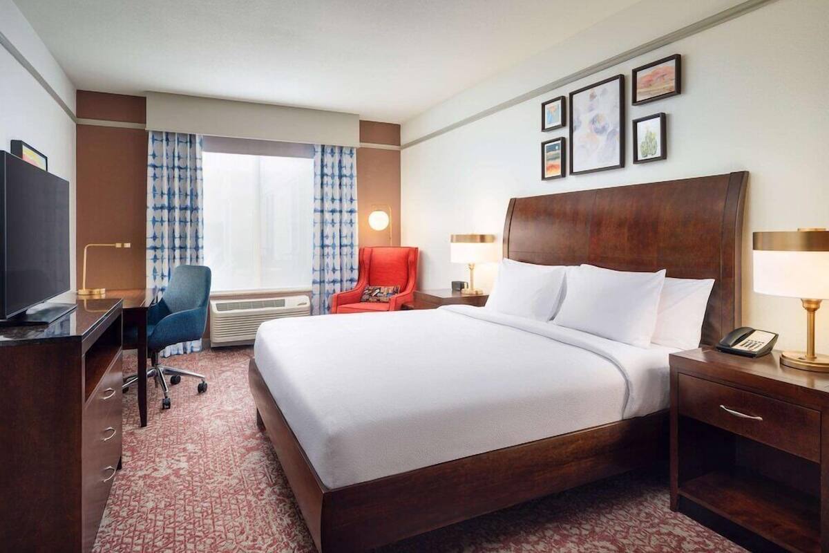A hotel room with a large bed, a desk, a chair, a TV, a lamp, and a telephone.