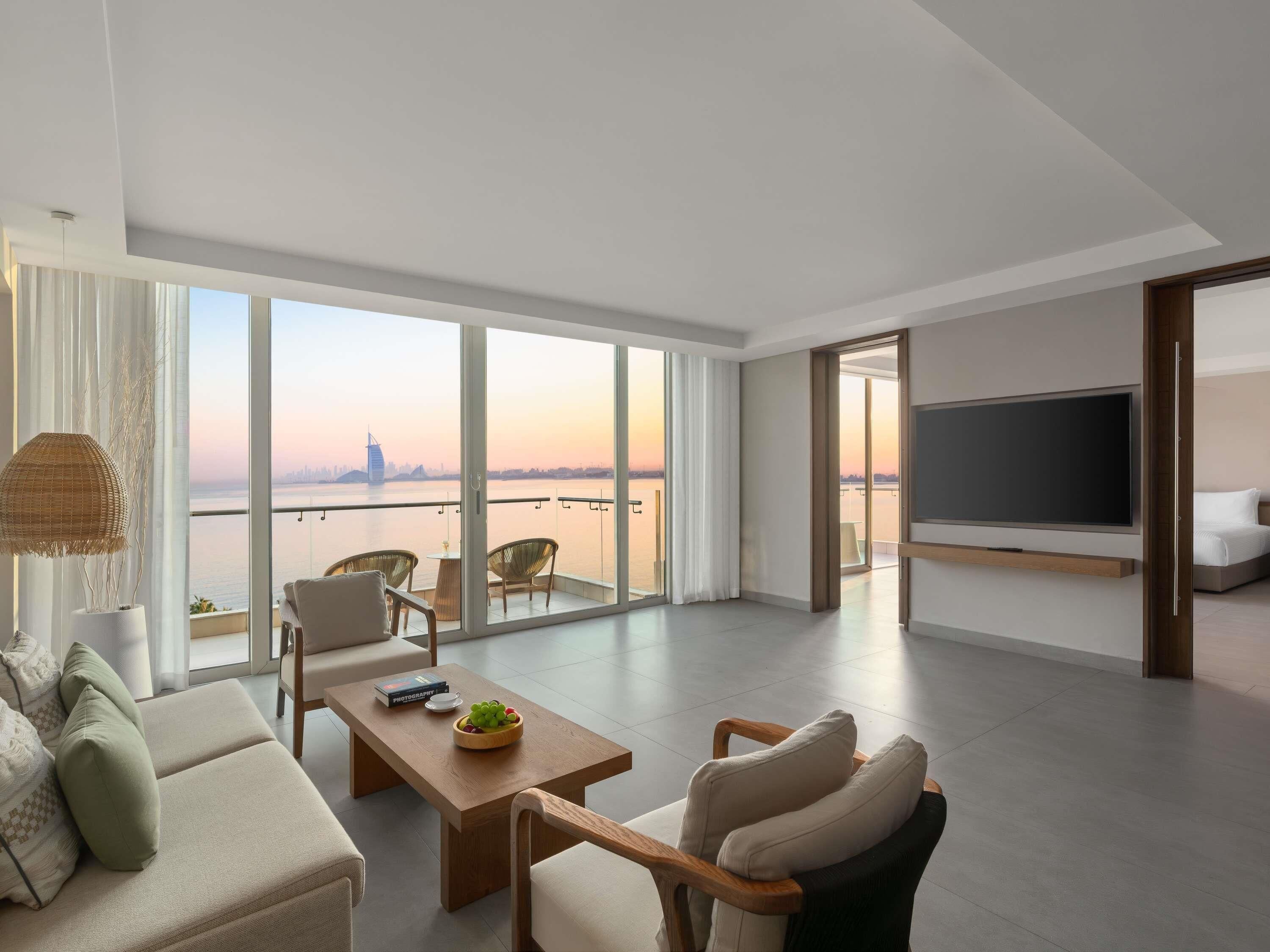 A modern living room with a large window, a flat-screen TV, a sofa, and a dining table.