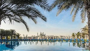 A poolside view with lounge chairs and palm trees, a city skyline in the background, and a clear sky. - Rixos The Palm Hotel & Suites – Ultra All Inclusive (Dubai)