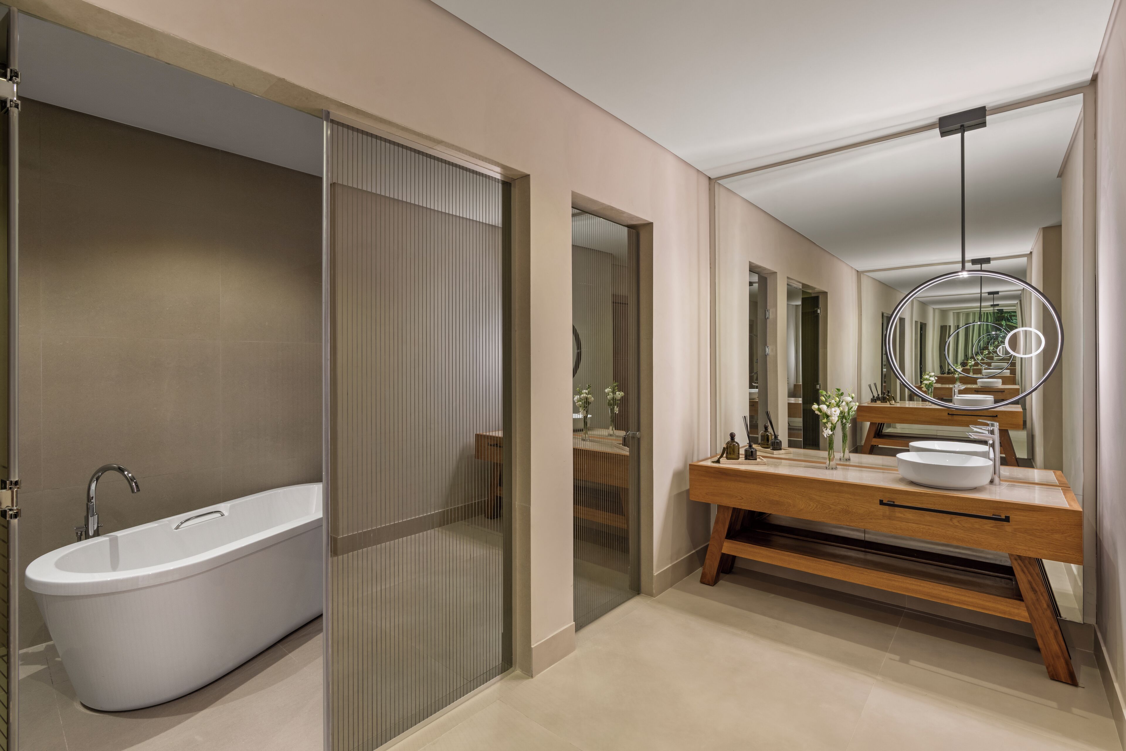 A modern bathroom with a freestanding bathtub, a wooden vanity with a large mirror, and a circular light fixture.