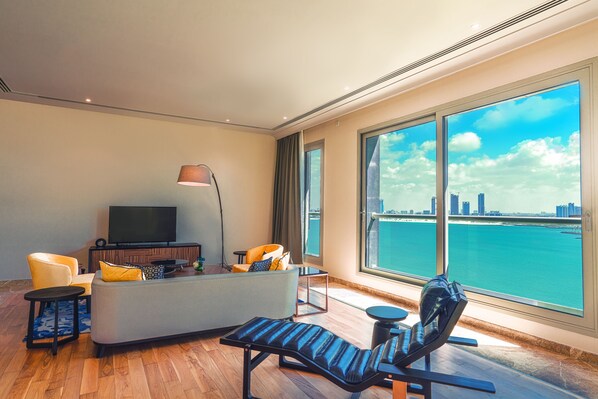 A modern living room with a sofa, armchair, and TV, large windows with a city view, and wooden flooring. - Rixos The Palm Hotel & Suites – Ultra All Inclusive (Dubai)