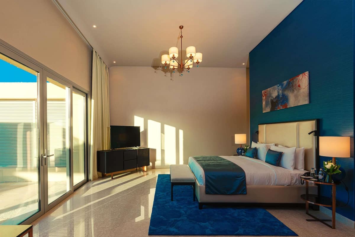 A modern bedroom with a large bed, a TV, a chandelier, and a painting on the wall.