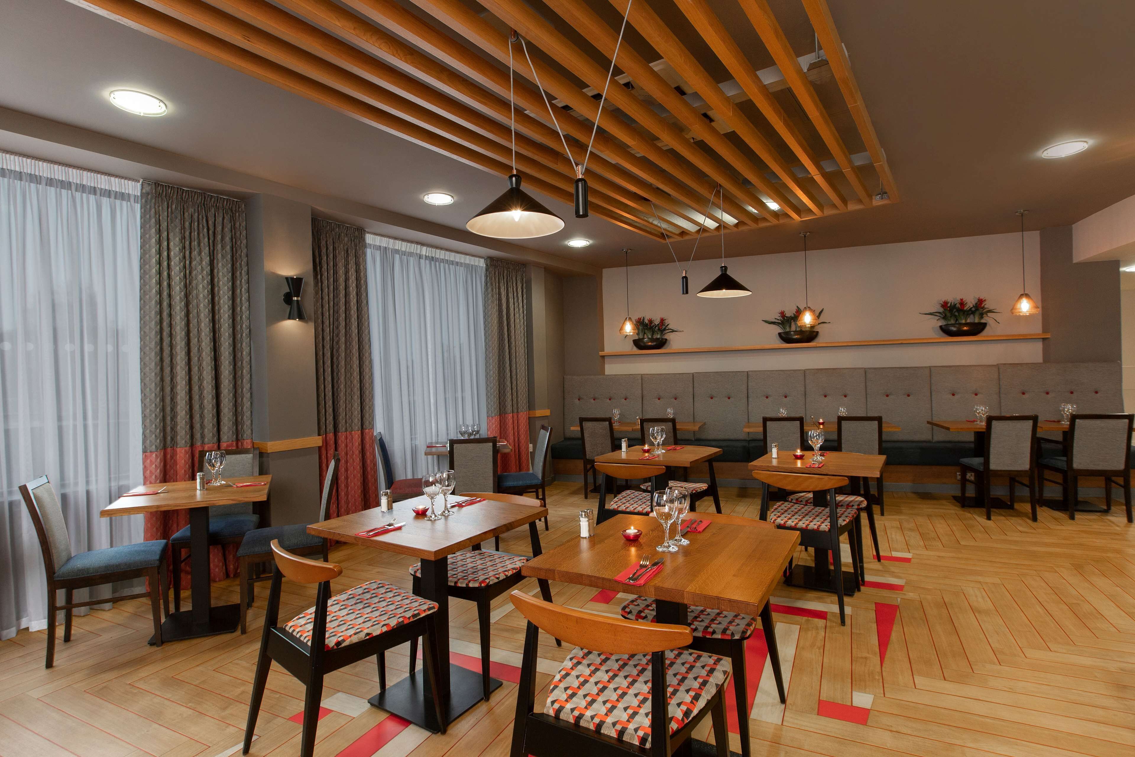 Un espace repas avec des tables et des chaises en bois, un éclairage au plafond et une palette de couleurs neutres.