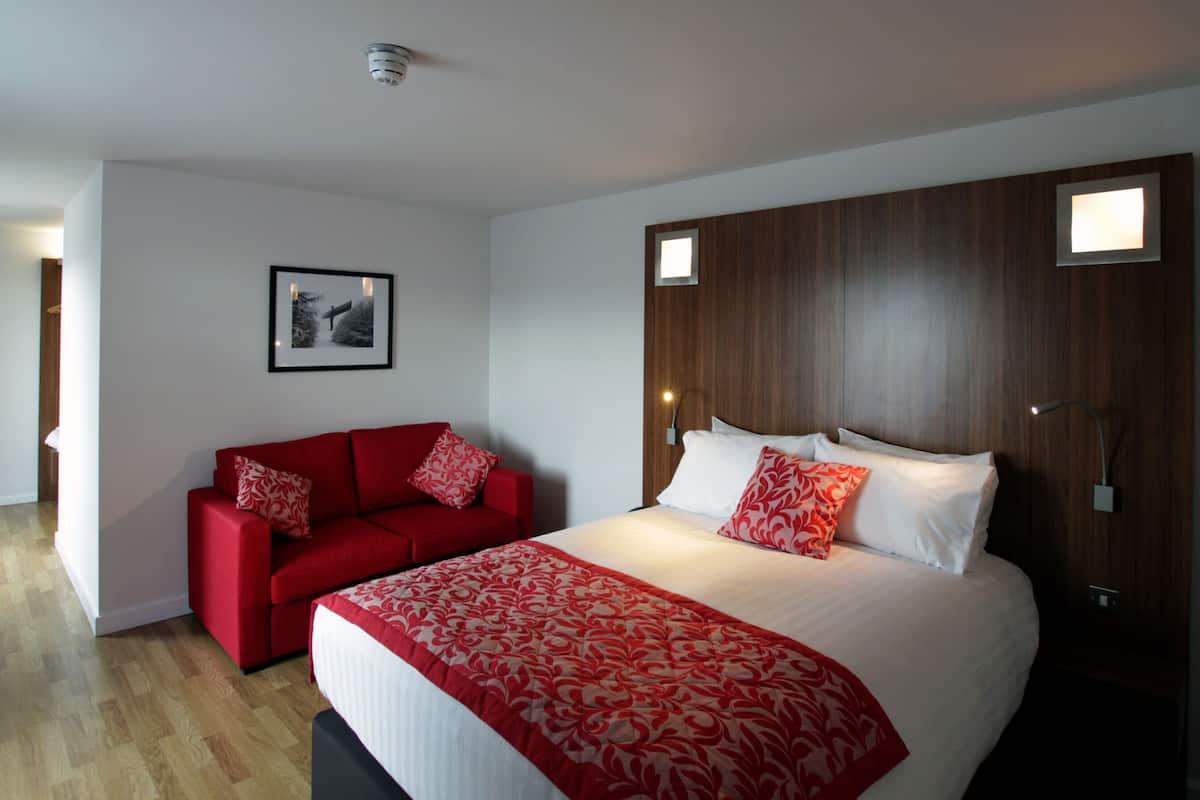 A hotel room with a large bed, a red sofa, a framed picture on the wall, and a wooden headboard.